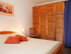 Ein Schlafzimmer mit einem Bett, orangefarbenen Kissen, einem Holzschrank, einem Stuhl und einem Bild an der Wand.
