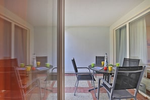 A balcony with a table and chairs, a small table with a lighthouse model, and a window with sheer curtains. - Apartment at Likedeeler Holiday Park (Ostseebad Boltenhagen)