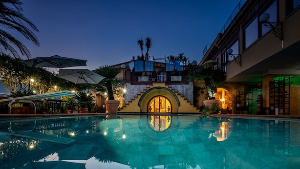 A swimming pool with a reflection of the building's architecture, including a balcony and palm trees. - Villa Amalia Resort (Cava de' Tirreni)