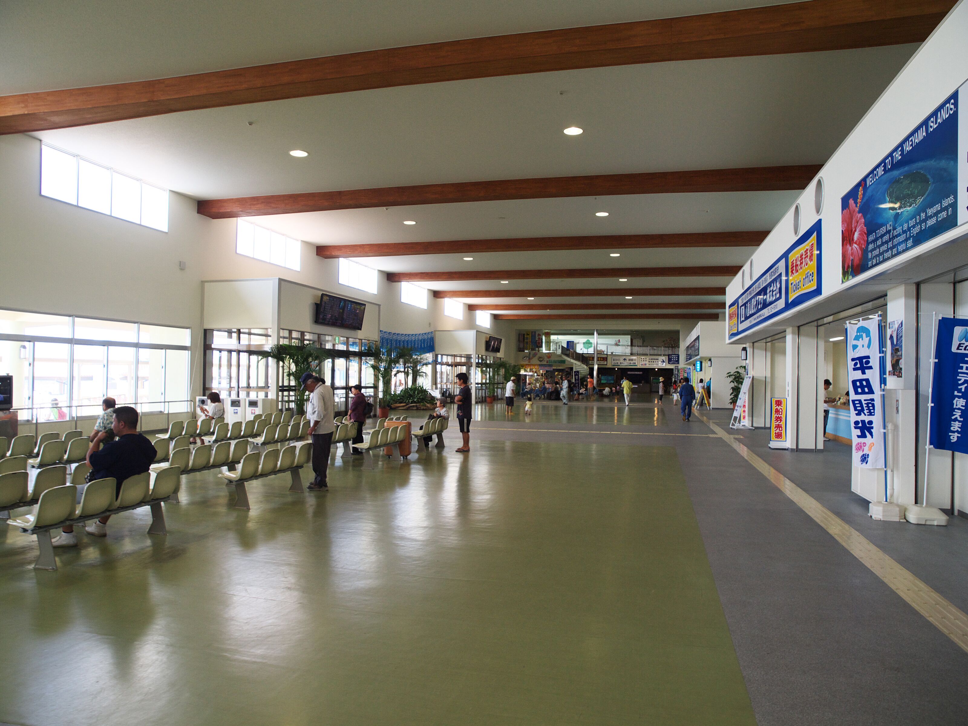 A spacious indoor area with rows of seating, a ticket office, and a staircase leading to an upper level.
