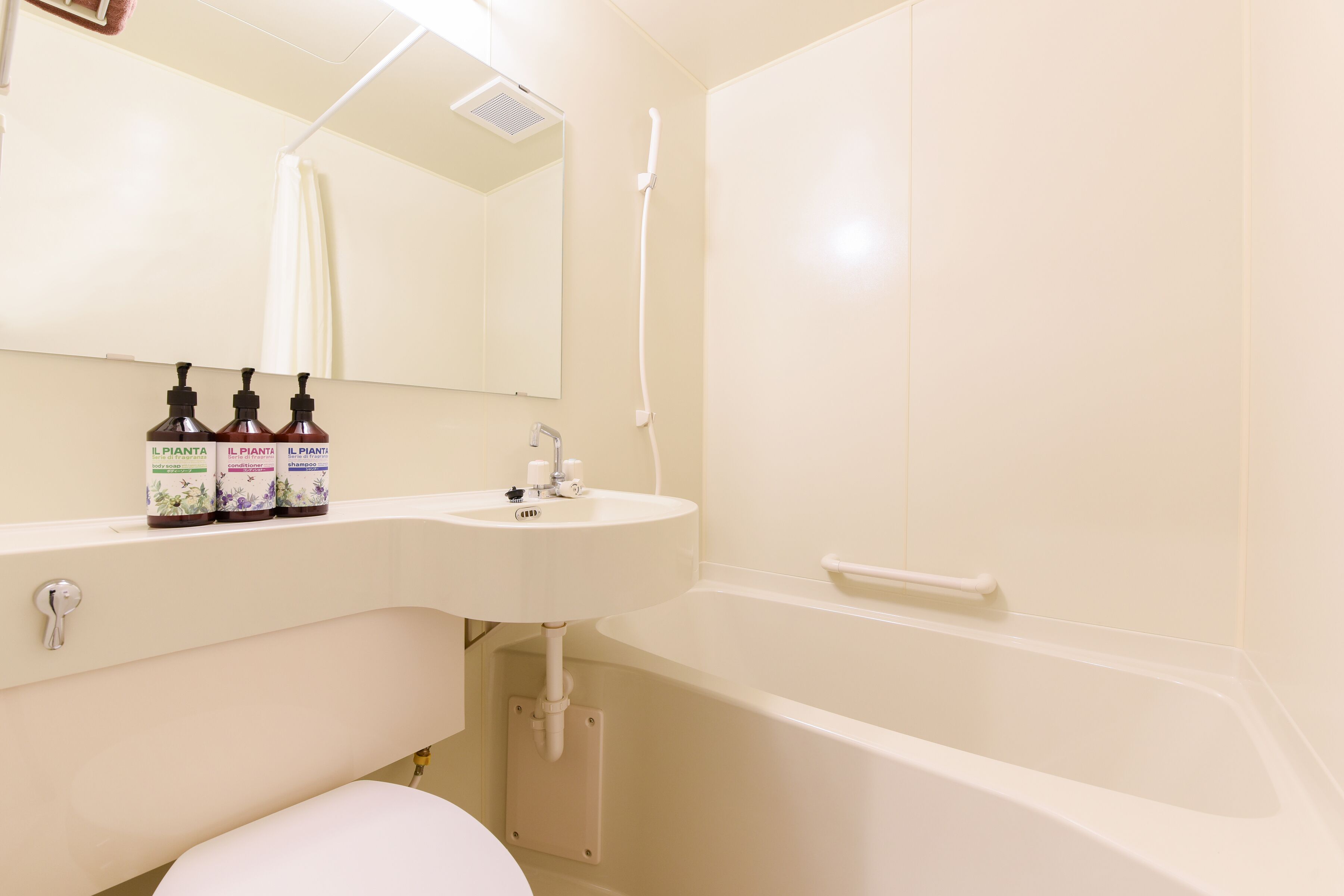 A bathroom with a sink, mirror, three bottles of L'PIANTA, a shower, and a toilet.