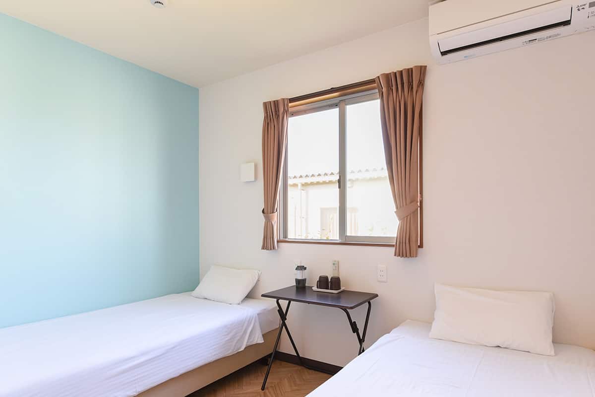 A room with two single beds, a small table with a kettle, and an air conditioning unit.