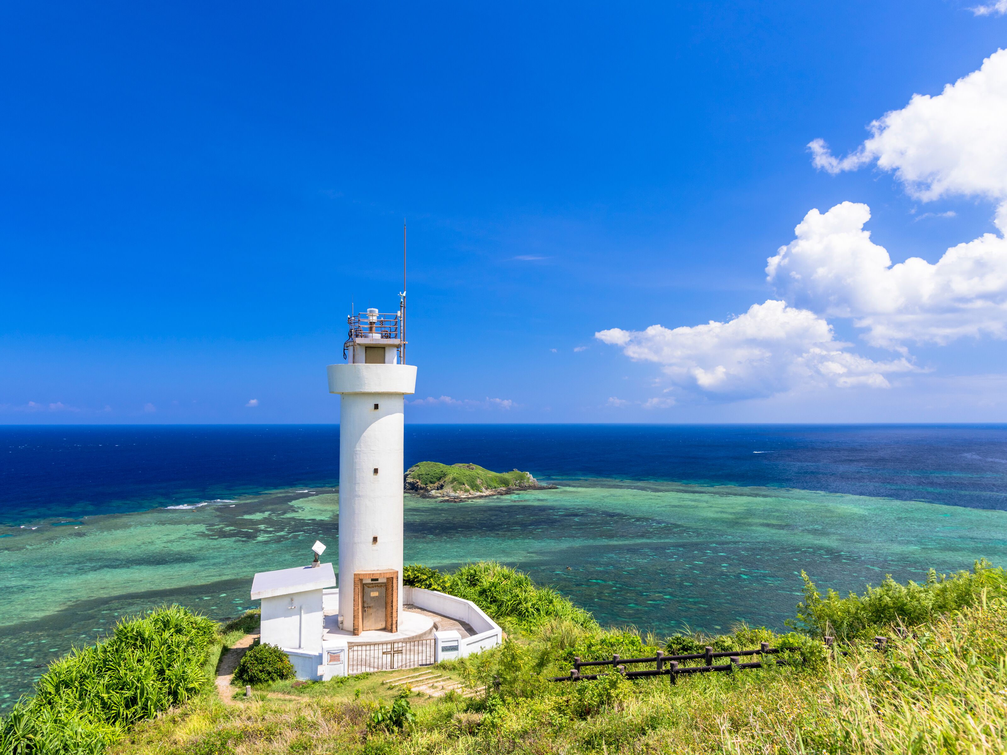 A lighthouse with a clear view of the ocean and a small island in the background.