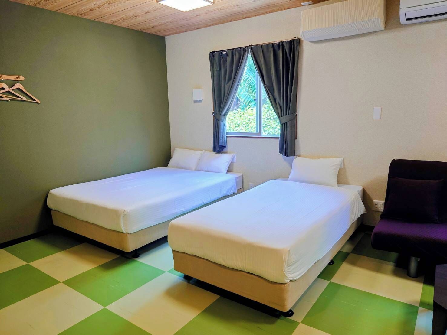 Une chambre avec deux lits simples, une fenêtre avec des rideaux, un plafond en bois et un sol à carreaux.