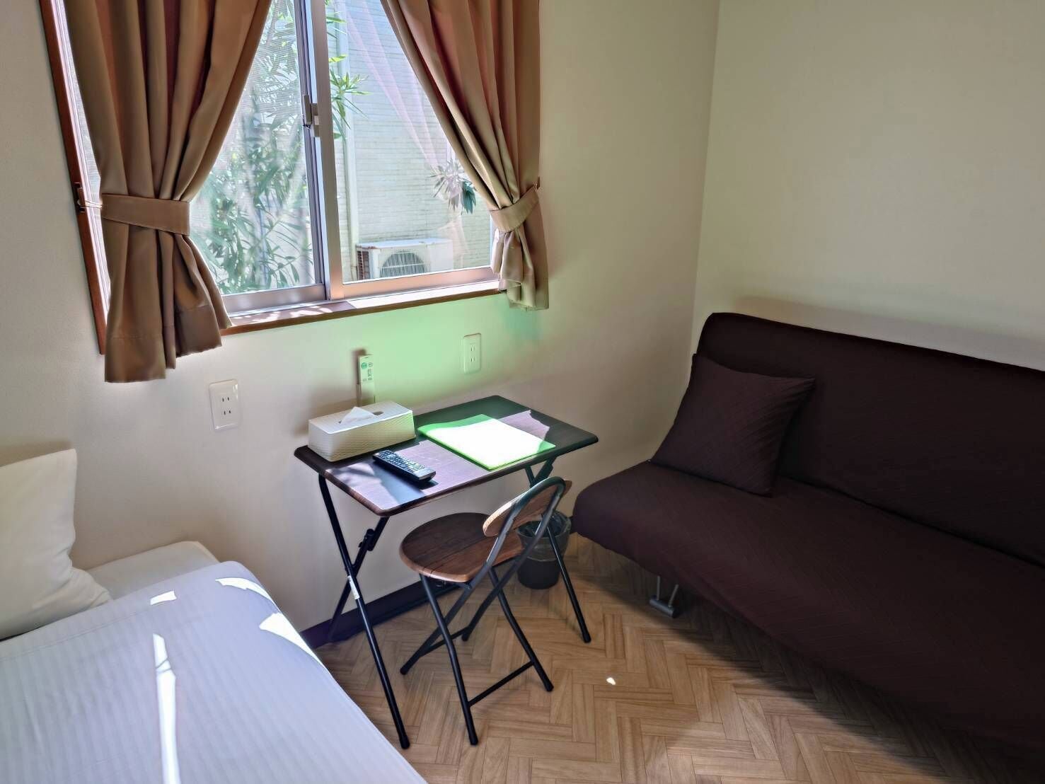 Une petite pièce comprenant un lit, un bureau avec une chaise, un canapé et une fenêtre avec des rideaux.