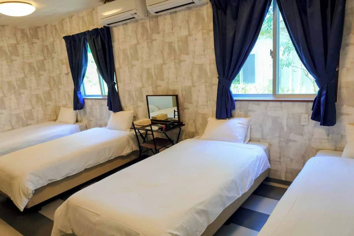 A room with two single beds, a desk with a chair, and a window with curtains.