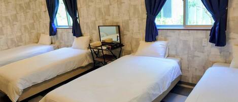 A room with two single beds, a desk with a chair, and a window with curtains.