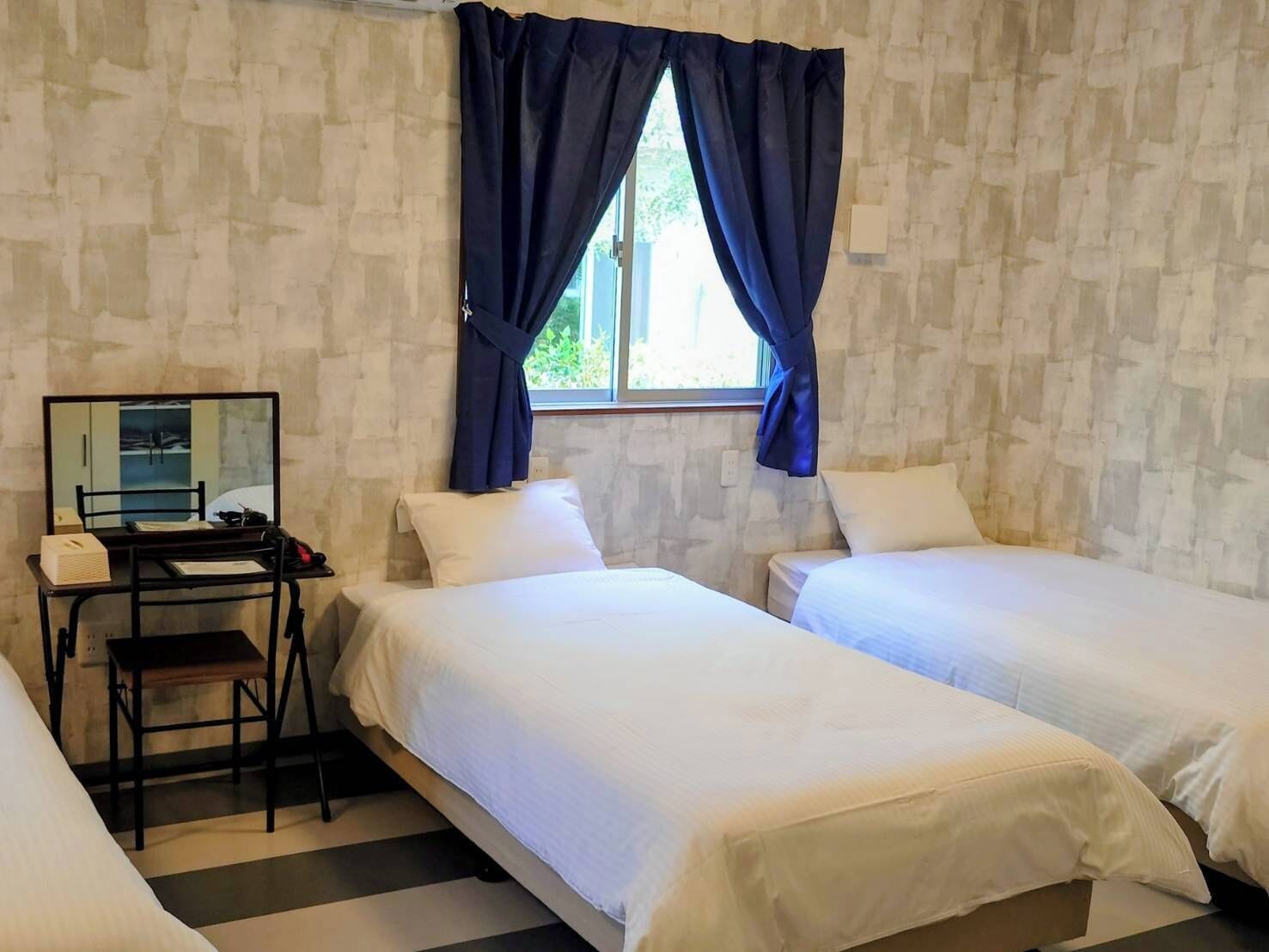A room with two beds, a desk with a mirror, and a window with curtains.