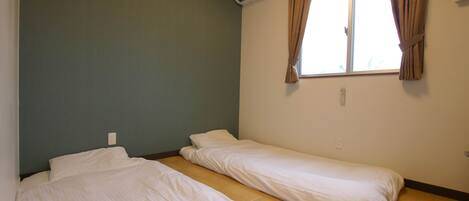 Una habitación con dos camas individuales, una ventana con cortinas, un equipo de aire acondicionado y un interruptor de luz en la pared.