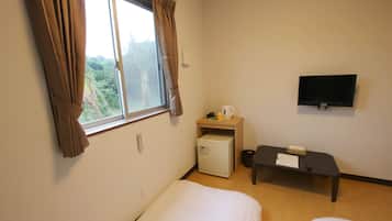 Una habitación de hotel con una cama, un escritorio pequeño, un televisor y una ventana con cortinas.