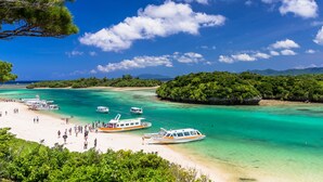 A beach with clear turquoise waters, boats, and a crowd of people.