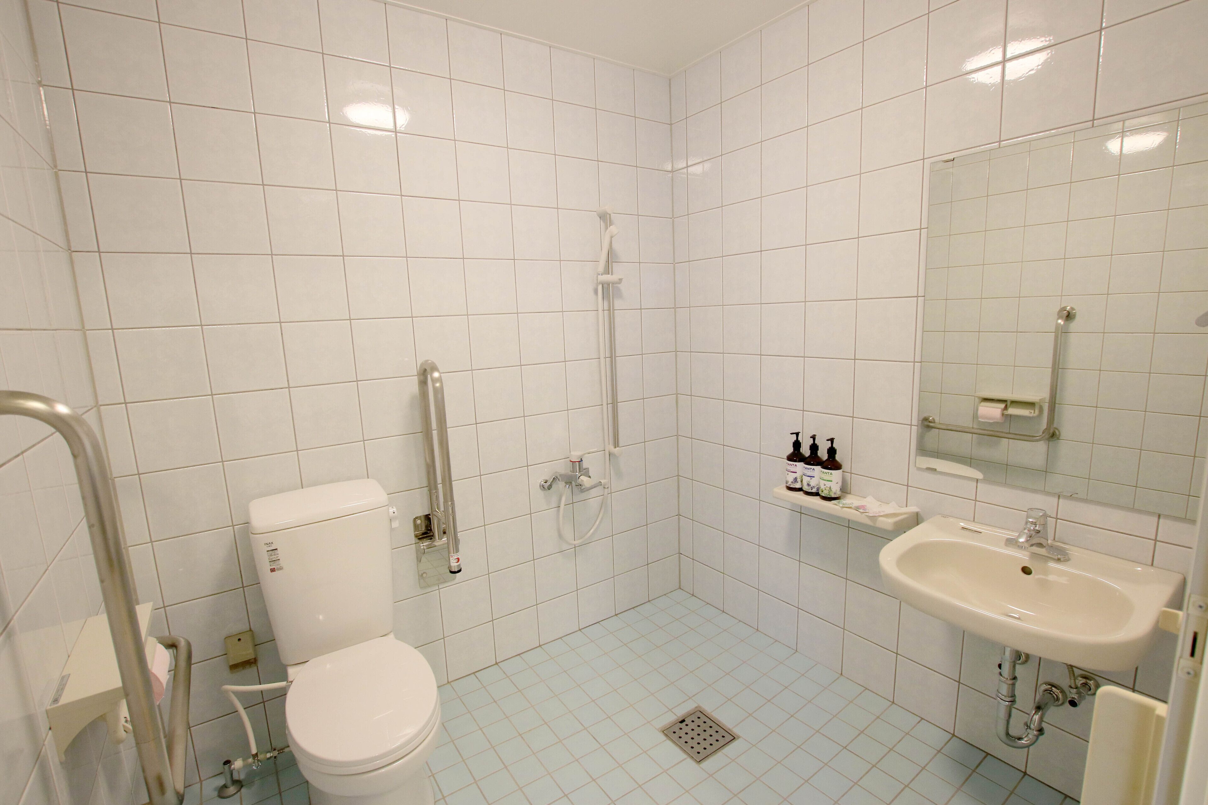 A bathroom with white tiles, a toilet, a shower, a sink, and a mirror.