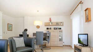 Un soggiorno moderno con un tavolino in vetro, una poltrona, una televisione e un'area pranzo con sedie, con una cucina sullo sfondo.