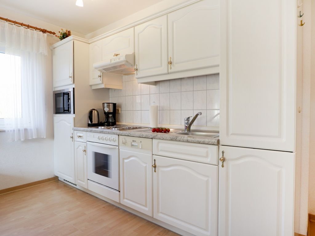 Een moderne keuken met witte kastjes, een inbouwoven, een koffiezetapparaat en een spoelbak.