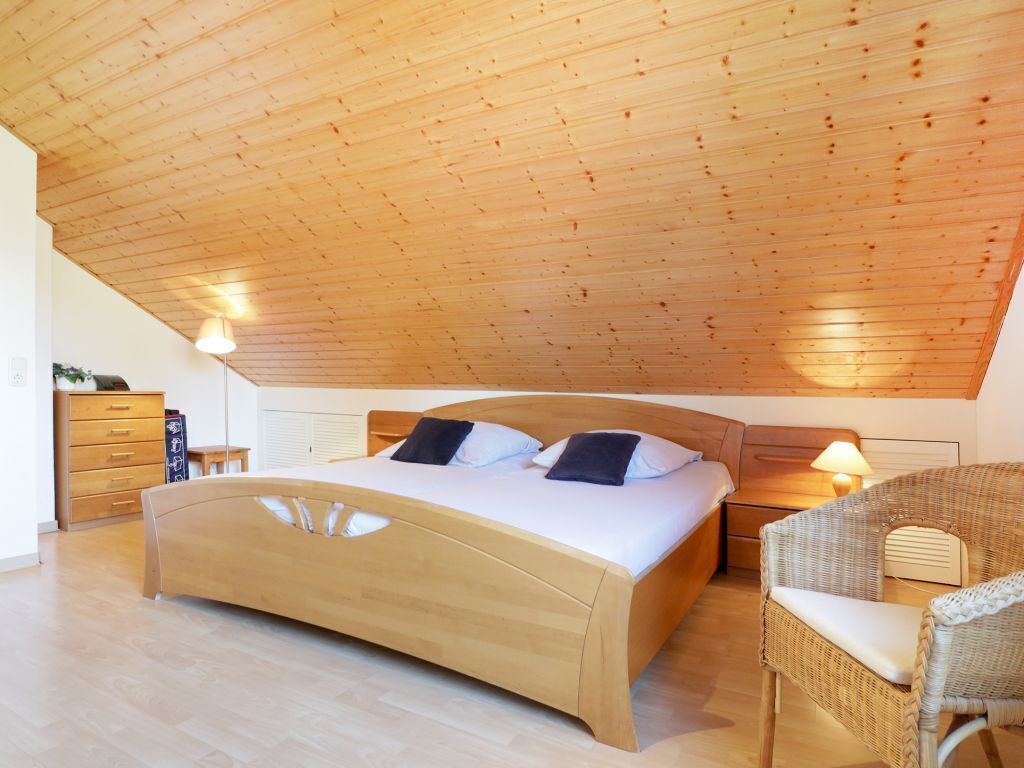A bedroom with a wooden ceiling, a bed, a nightstand, a chair, and a dresser.