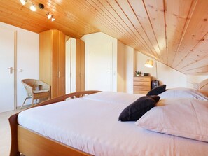 A bedroom with a wooden ceiling, a bed with white and black bedding, a chair, and a dresser. - Vacationer village 20c, Germany (Ostseebad Boltenhagen)