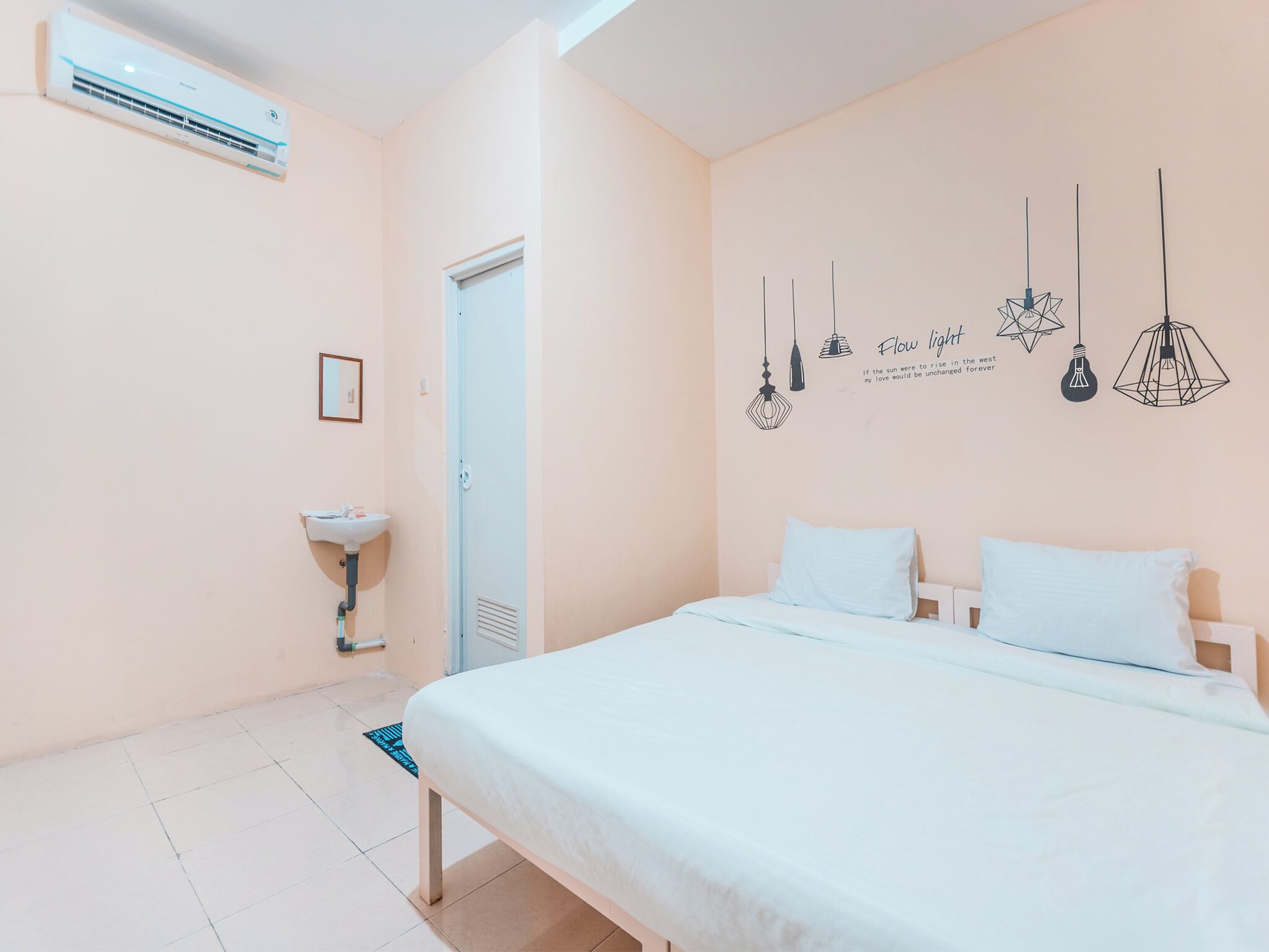 Une chambre à coucher comprenant un lit, une table de chevet, un climatiseur fixé au mur, un luminaire fixé au mur et une porte.
