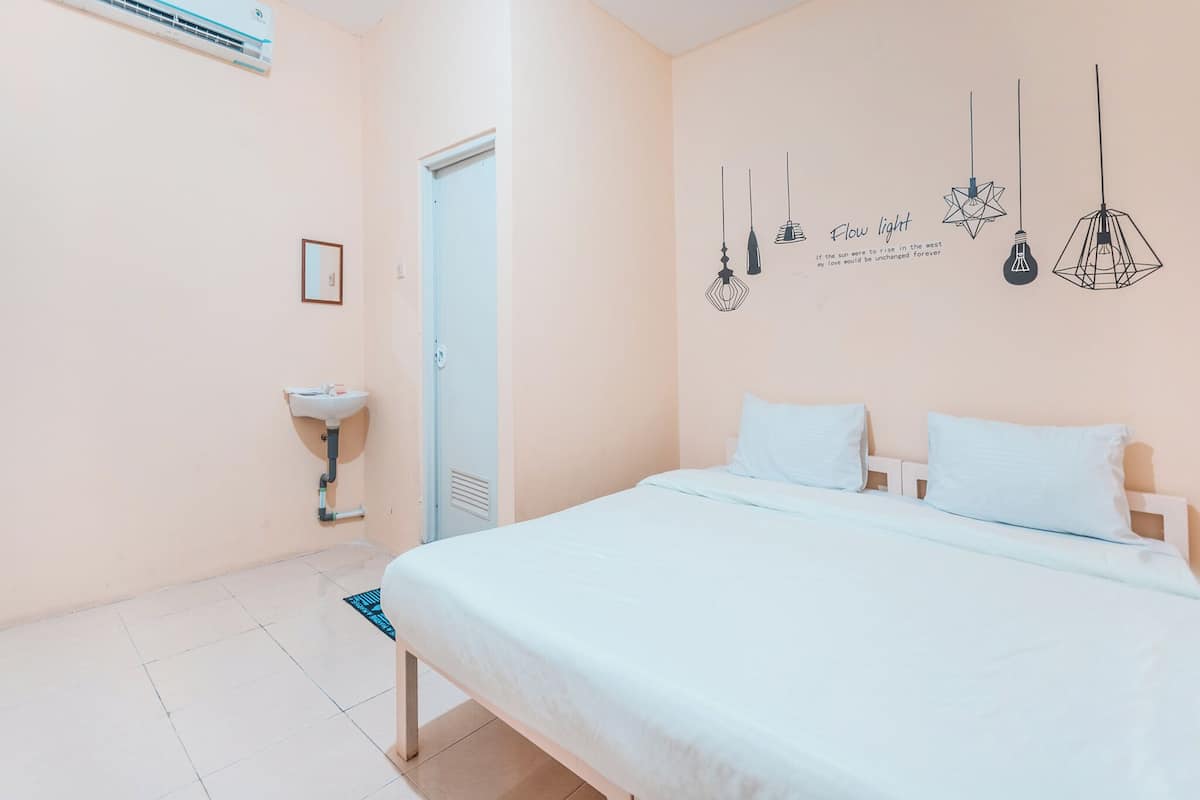 A bedroom with a bed, a bedside table, a wall-mounted air conditioner, a wall-mounted light fixture, and a door.