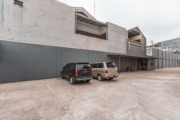A parking area with two SUVs parked next to a building with a concrete facade and a metal balcony.