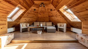 A cozy attic room with wooden walls and a sloped ceiling. It features a sofa, a table, and two chairs. - Willa Galantowka (Zakopane)