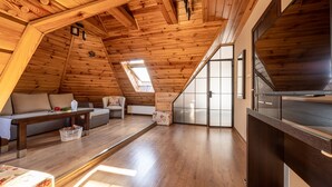 A cozy attic bedroom with wooden beams, a skylight, a sofa, a chair, and a TV. - Willa Galantowka (Zakopane)