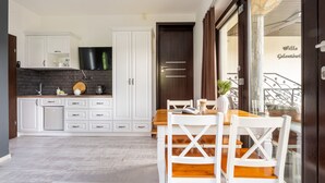 A modern kitchen with white cabinetry, a black countertop, and a dining area with a wooden table and white chairs. - Willa Galantowka (Zakopane)