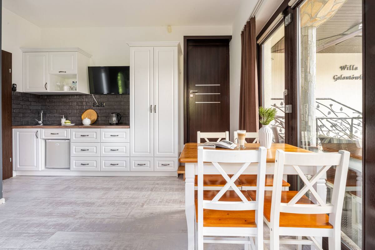A modern kitchen with white cabinetry, a black countertop, and a dining area with a wooden table and white chairs.