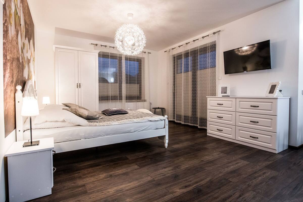 A bedroom with a bed, dresser, TV, and a chandelier.
