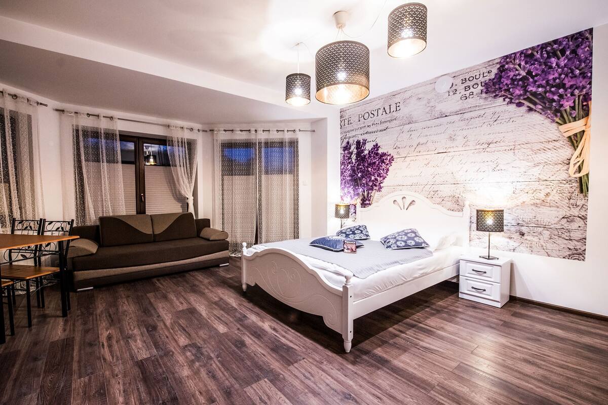 A bedroom with a bed, bedside tables, a sofa, a dining table, and curtains.