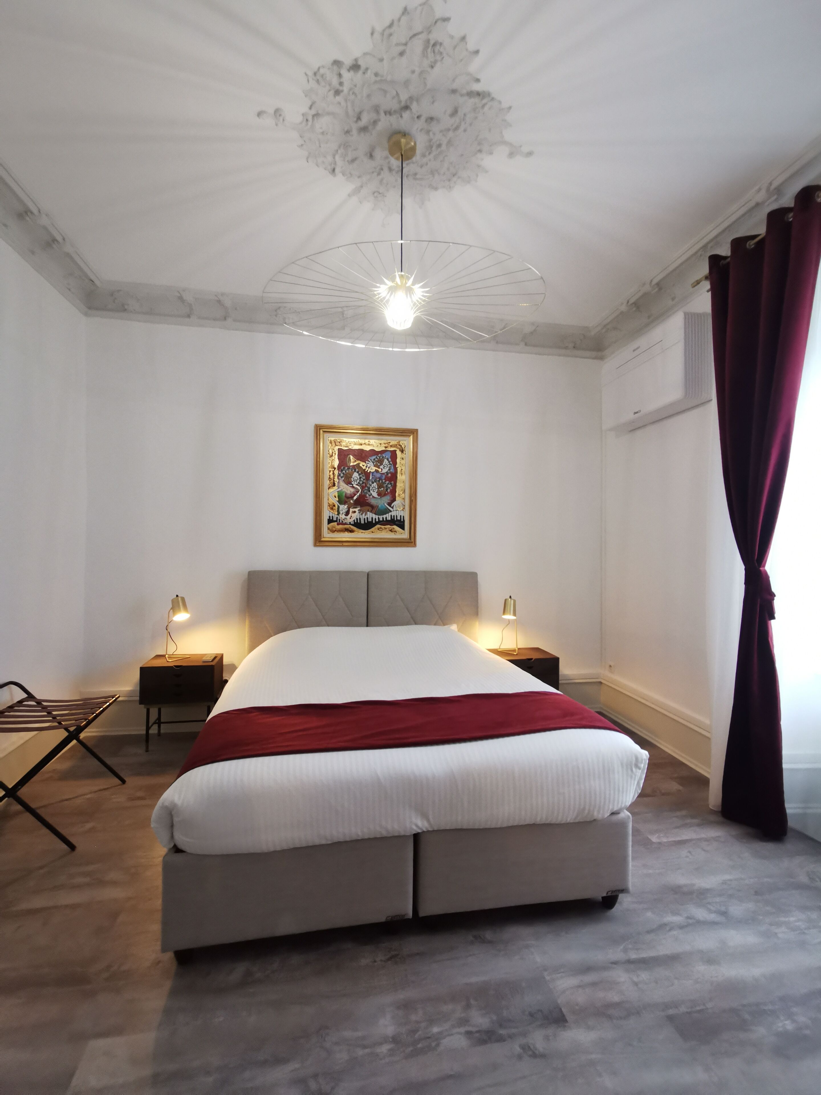 Un dormitorio moderno con una cama grande, dos mesitas de noche con lámparas, un accesorio de iluminación en el techo y una obra de arte enmarcada en la pared.