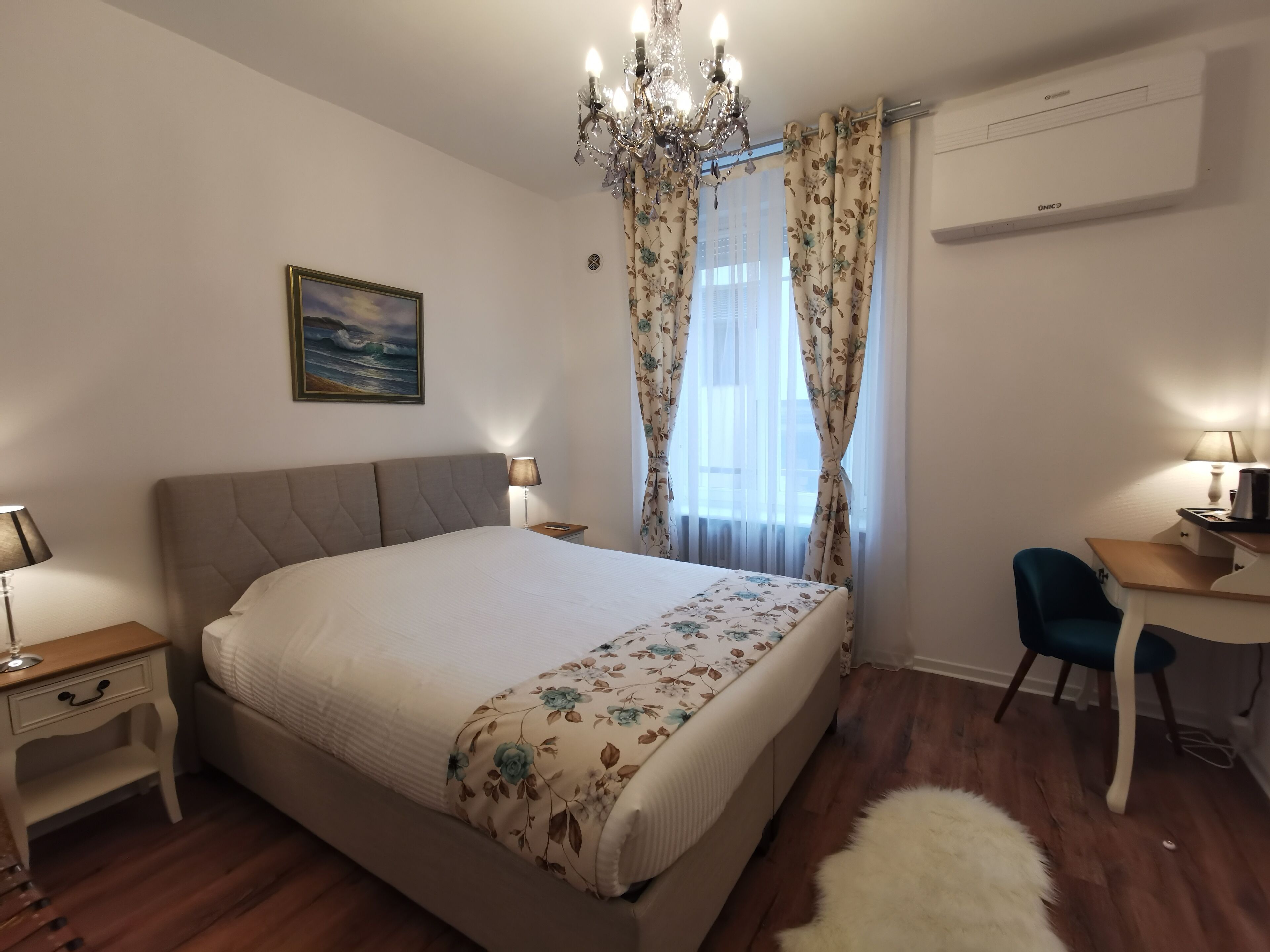 Une chambre à coucher avec un lit, un bureau, une chaise, un lustre et un tableau au mur.