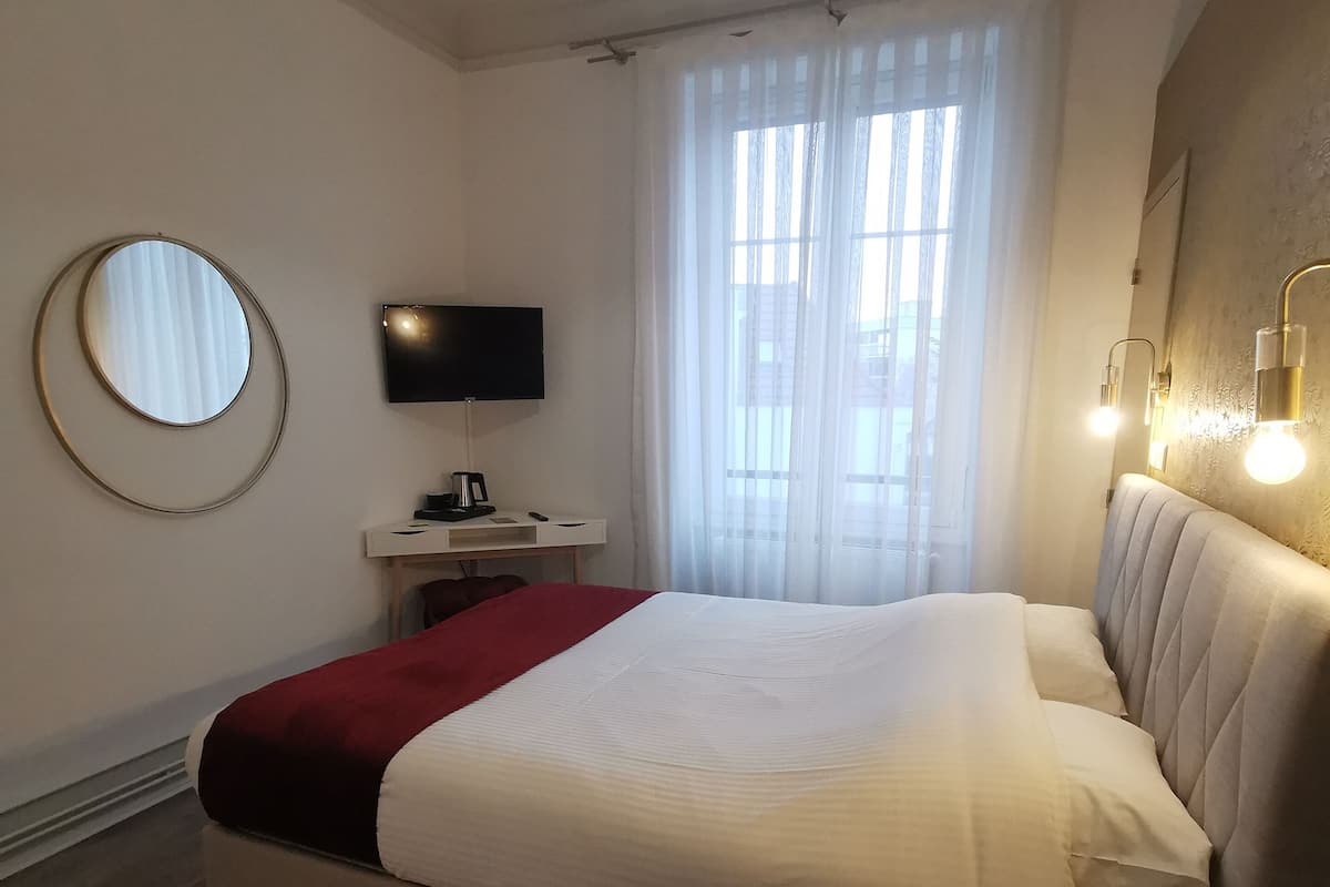 A neatly arranged bedroom with a bed, a television, a desk, and a window with curtains.