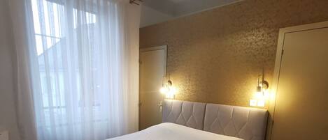 A large bed with a red throw blanket, a hanging light fixture, and two wall-mounted lights.