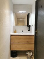 Un baño moderno con lavamanos blanco, cajones de madera, un espejo y un secador de pelo negro.