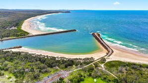 Vista aérea de uma área costeira com praia, molhe e vegetação ao redor.