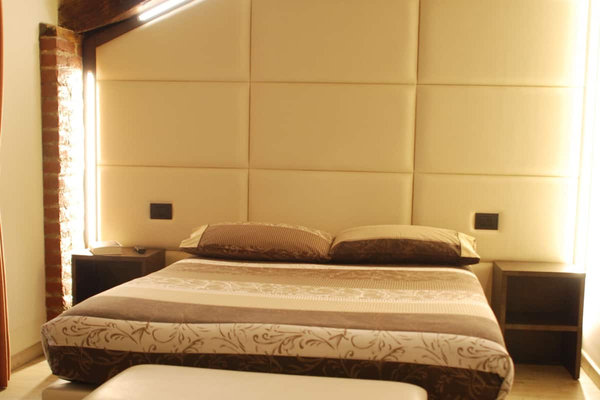 A bedroom with a large bed, a bench, wooden headboard, and a nightstand.