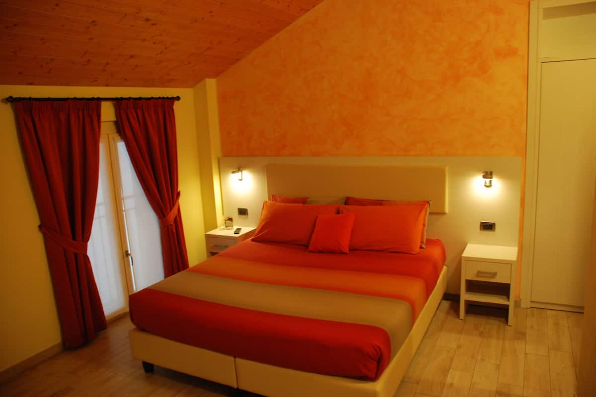 A bedroom with a large bed, red curtains, wooden flooring, and two bedside tables with lamps.