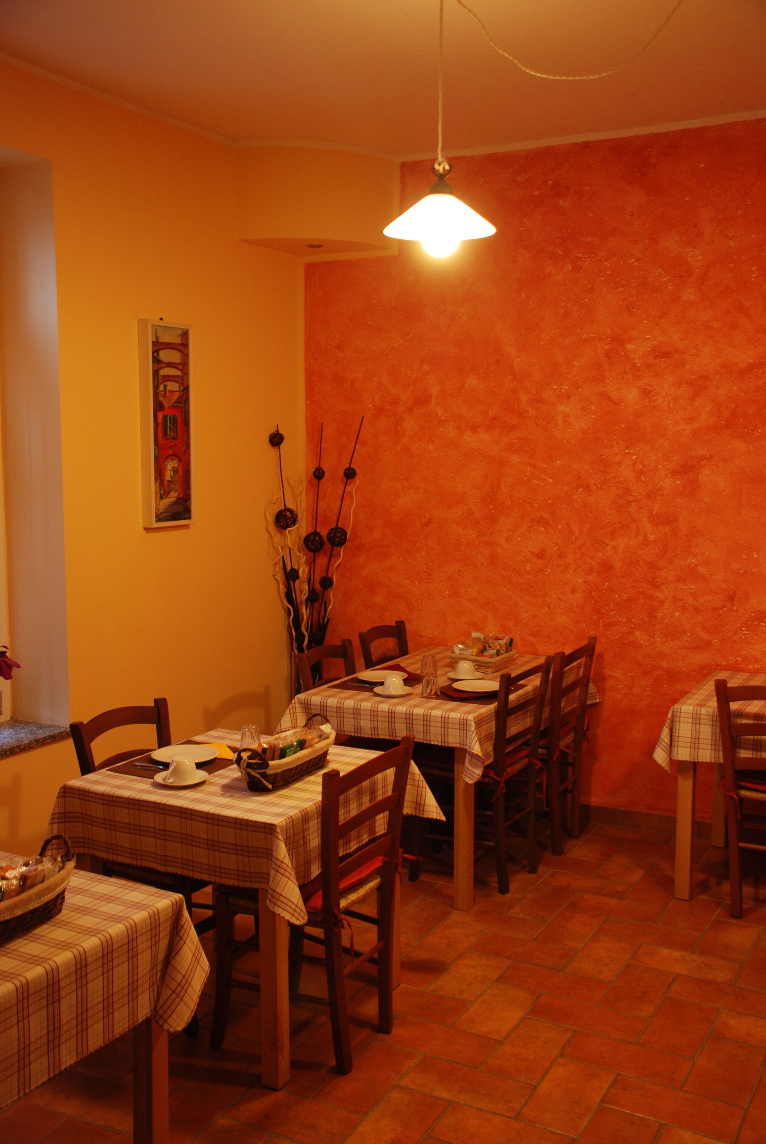 A dining area with multiple tables and chairs, a hanging light fixture, and a wall-mounted painting.