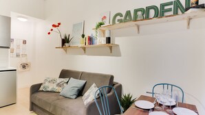 Ein modernes Wohnzimmer mit einer Couch, einem Esstisch für vier Personen und einer Küche im Hintergrund.