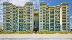 A high-rise hotel with multiple balconies, located near a beach.