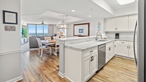 A modern kitchen with white cabinetry, a central island, and a dining area with a table and chairs.