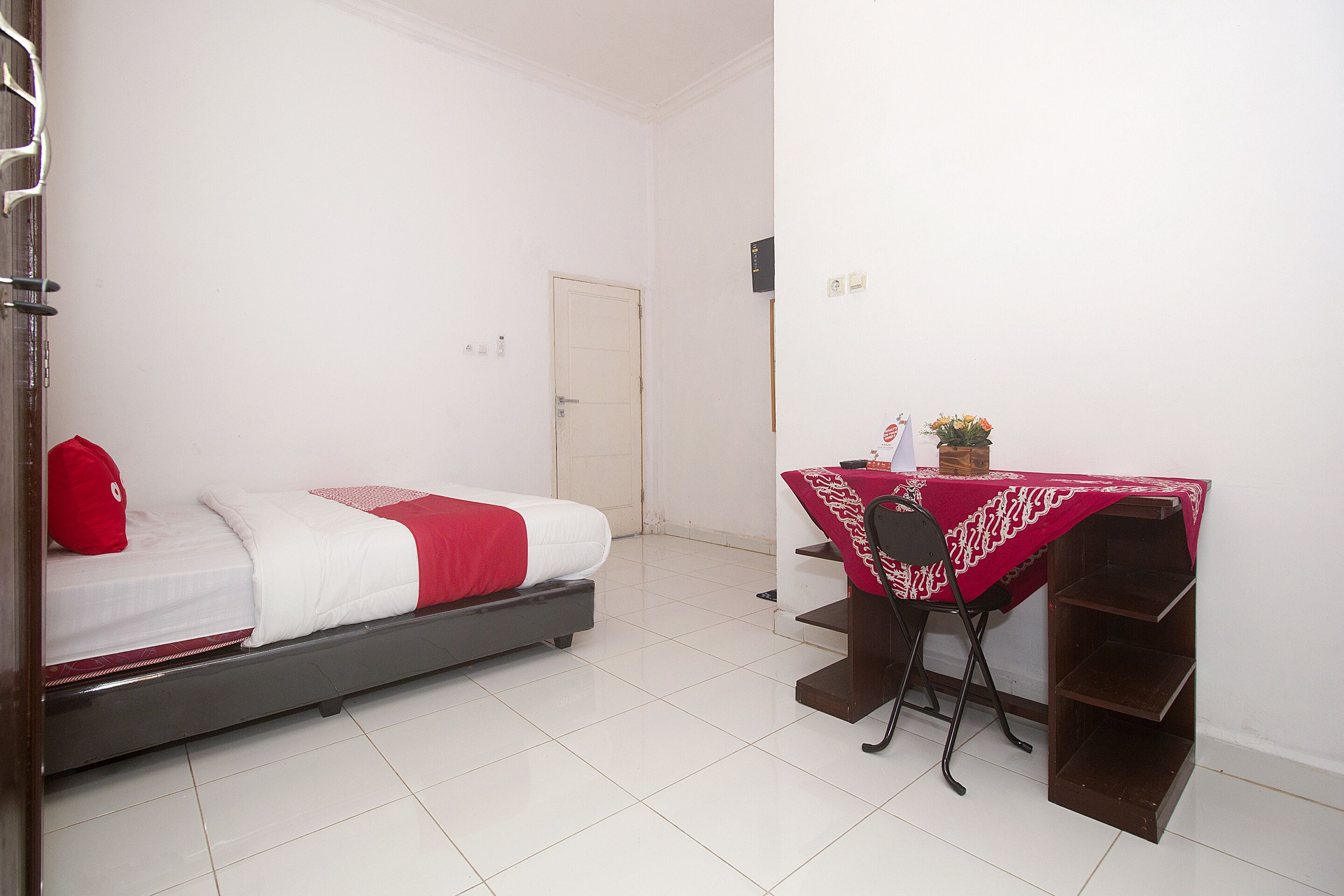 Un dormitorio con una cama, un escritorio con mantel rojo y una silla.