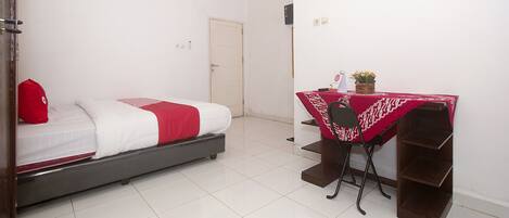 Un dormitorio con una cama, un escritorio con mantel rojo y una silla.