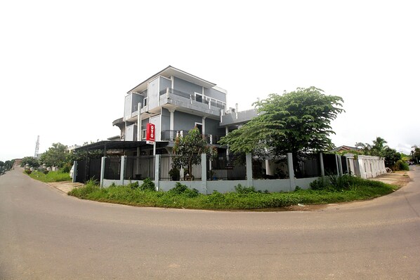 A two-story building with a balcony, surrounded by greenery and a gated fence.