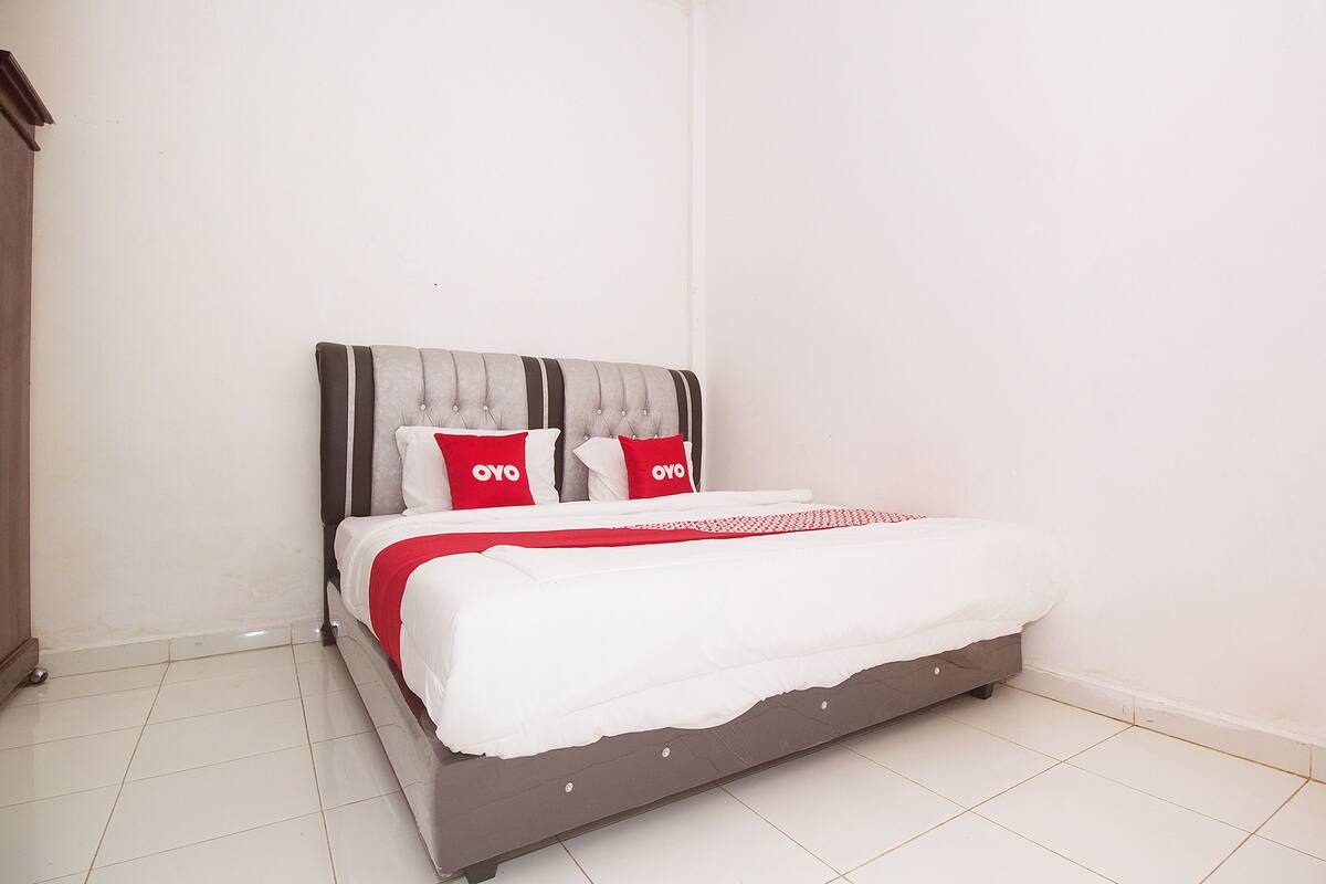A bed with a grey headboard, white bedding, and red pillows with the brand "OYO" on a white tiled floor.