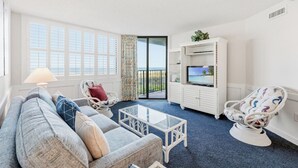 Una sala de estar con un sofá, dos sillones, una mesa de centro, un televisor sobre un mueble y vista al océano.