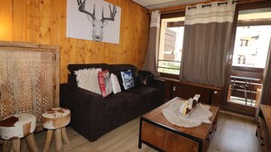 Una stanza con pannelli in legno, un divano marrone scuro, due sgabelli di legno, un tavolino da caffè e un quadro appeso al muro raffigurante un cervo.