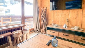 Interno in legno con TV a parete, mobili in legno e finestra con vista su posti a sedere all'aperto.