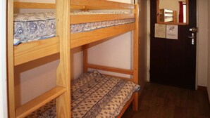 Ein Mehrbettzimmer mit Holzbettgestell, gemusterten Betttextilien und einer Tür mit Spiegel und Schildern.