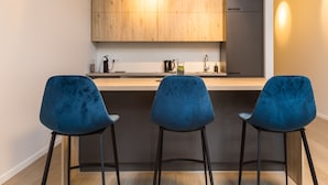 Une cuisine moderne avec des meubles en bois, un réfrigérateur gris et trois tabourets de bar bleus.